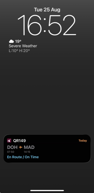 A Voyageur flight's live status on the iPhone Lock Screen, showing route, times, and En Route status